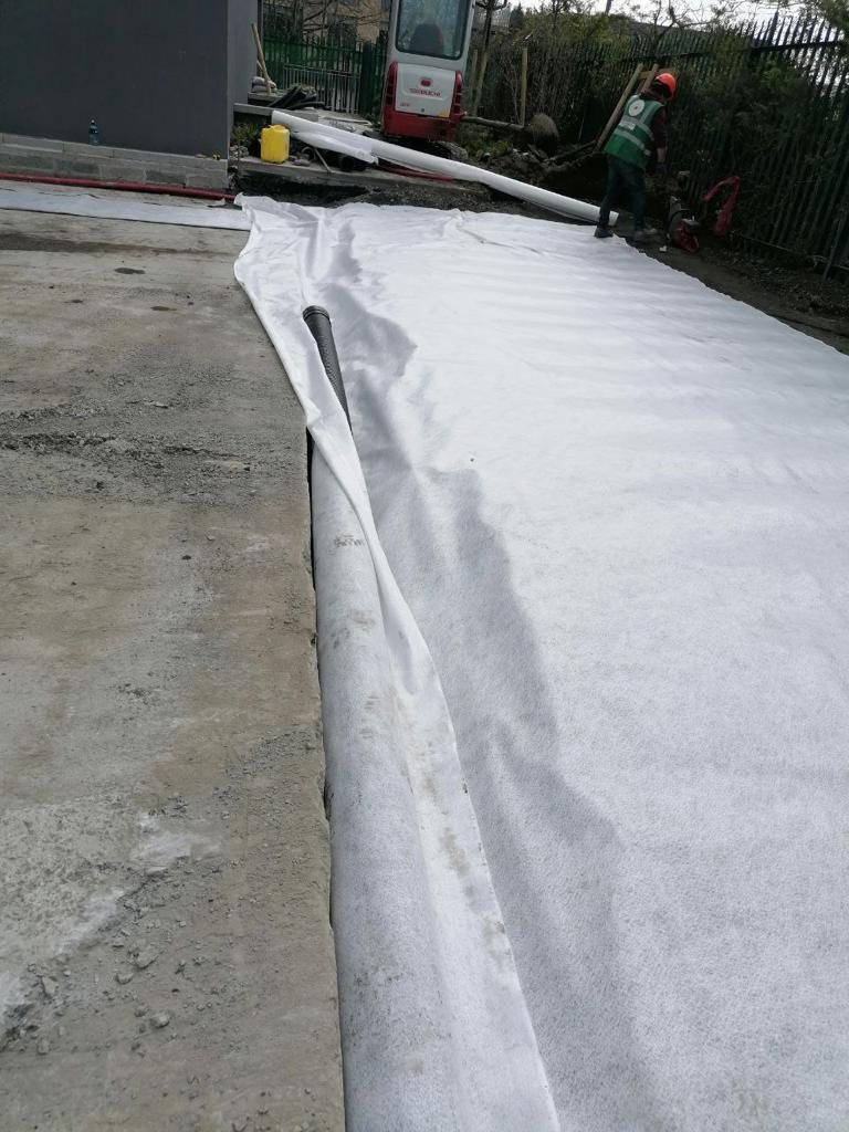 A person laying out a white fabric next to a red truck in an industrial area